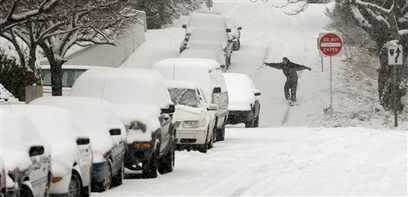 A snowboarder heads down a side street and past snowed-in cars ...