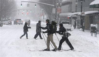 A couple uses skis to cross a snowy street in downtown Portland, ...